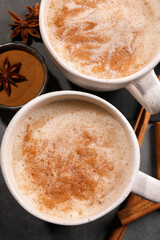 Cups of delicious eggnog with anise and cinnamon on grey table, flat lay