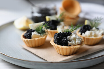 Delicious tartlets with black caviar, cream cheese and lemon served on light table, closeup