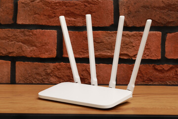 New white Wi-Fi router on wooden table near brick wall