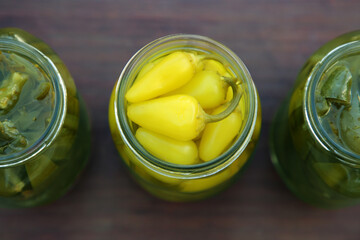Glass jars of pickled green and yellow jalapeno peppers on wooden table, flat lay