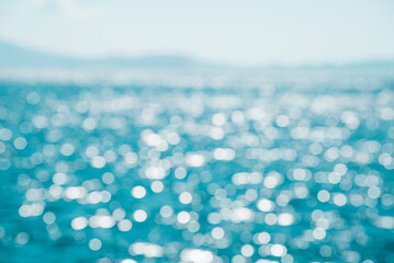 Blurred background of blue water and bokeh of sunlight hitting the sea with Mountain View and clear sky. Summer holiday backdrop.Mock up template for display or montage of product or content.