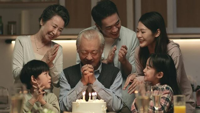 three generation asian family celebrating grandpa's birthday at home with cake and candle lights