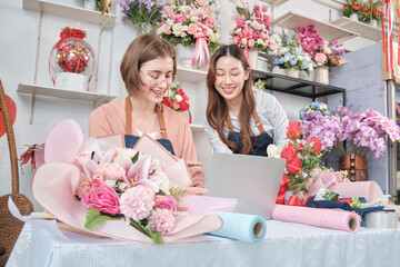 Two young beautiful female florist partners discuss flora bunch decoration, online purchase orders and website arrangement for business, happy work in colorful flower shop store, and e-commerce SME.