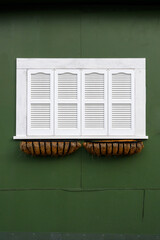 White wooden window shutters on the side of a dark green building
