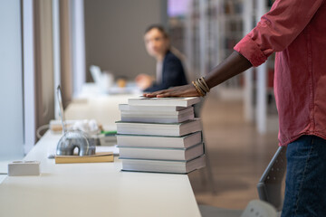 Close up of books and teaching aids taken by student on library bookshelves in pile stacked on...
