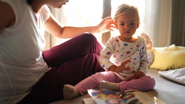 Mom tells the little girl about the book lying in front of her on the bed