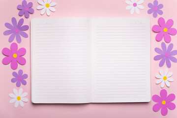 Páginas de diario en blanco con margaritas y flores de papel alrededor sobre fondo rosa