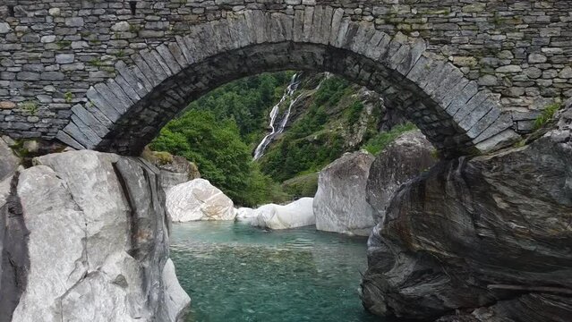 Ancient stone bridge over mountain river in Switzerland, aerial fly under and ascend view