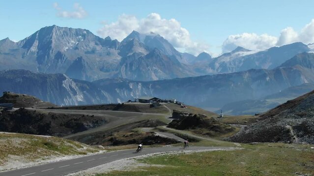 Couple of cyclists on Col de la Loze mountain pass with Alps in background, France. Aerial forward