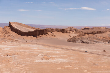 Fototapeta premium Car riding on a deserted road in the middle of Atacama Desert, Valle de la Luna, Moon Valley, Chile