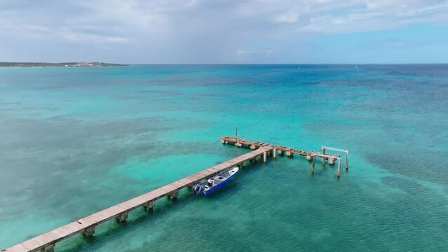 Aerial orbit shot of wooden jetty with parking motorboat on turquoise clear ocean water of Dominican Republic