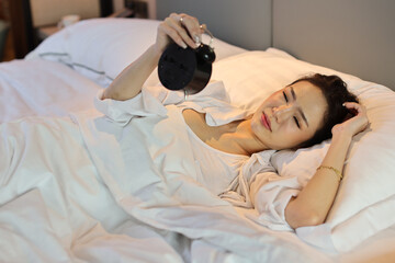 Happy young asian woman in white lingerie lying in bed, wake up late and overslept morning, trying to stop alarm clock. Cute girl look comfortable, need more sleep. Difficult morning get up concept