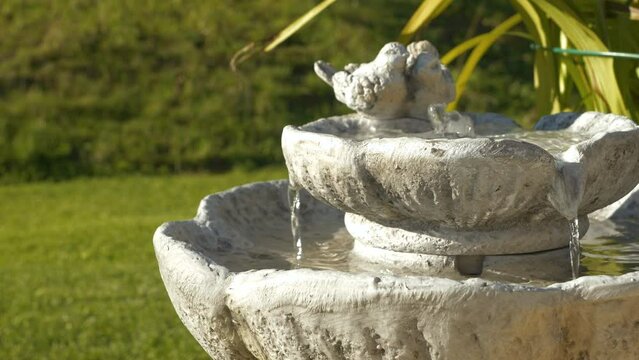 CLOSE UP: Decorative outdoor fountain with running water in green spring garden. Atmospheric garden water element with relaxing and calming effect. Cascading birdbath for hot and dry summer days.