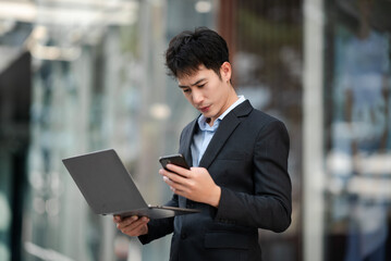 Asian businessman using a tablet and laptop  on a bench in the city