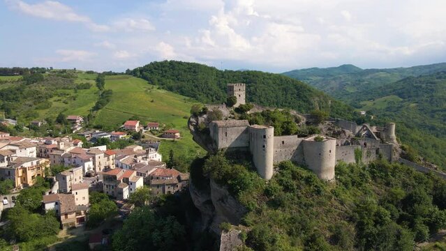 Drone shot orbiting a medieval castle on top of a cliff with tourists climbing to the summit and birds flying by. This ancient castle is located in Abruzzo Italy and is called Roccascalegna.