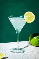 Vodka gimlet alcoholic cocktail drink with vodka, syrup, lime juice and ice, dark green background, bright hard light and shadow pattern