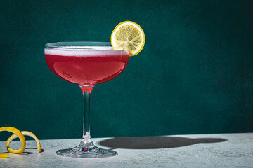 Pink lady alcoholic cocktail drink with gin, grenadine syrup, lemon juice and egg white, dark green background, bright hard light and shadow pattern