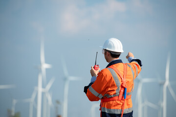 Engineer at Natural Energy Wind Turbine site with a mission to take care of large wind turbines Use a walkie talkie to communicate with a colleague working on top of the wind turbine.