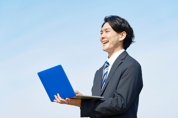 外でパソコンを使うビジネスマン　青空背景