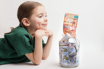 Happy girl with a large transparent jar with Kazakhstani tenge money on a white background.