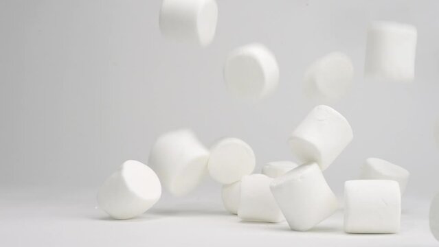 White jumbo gelatin marshmellows falling onto white tabletop and rolling around in slow motion