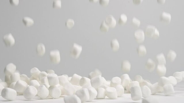 White miniature bite size marshmallow pieces falling onto white table top and bouncing around in slow motion