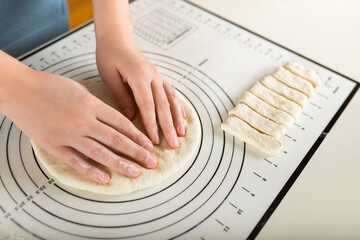 Close-up of hands kneading rolled out dough on a kitchen baking mat with round markings of...