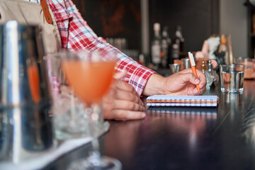 bartender standing at bar counter taking notes - 571456278