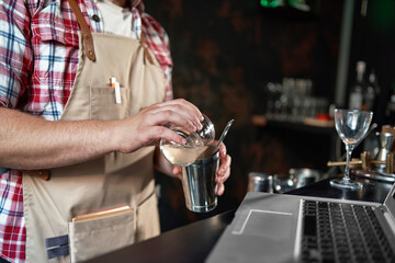 bartender pouring a cocktail from a shaker into a glass.