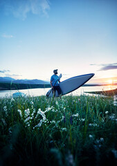 Man with SUP board near lake at sunset