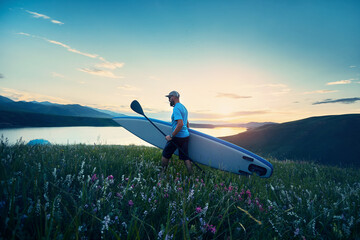 Man with SUP board near lake at sunset