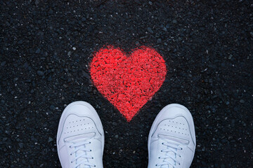 Grafitti red heart on black street background with white shoes stand in front, table top view