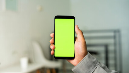 Hand holding green screen smartphone with living room backdrop