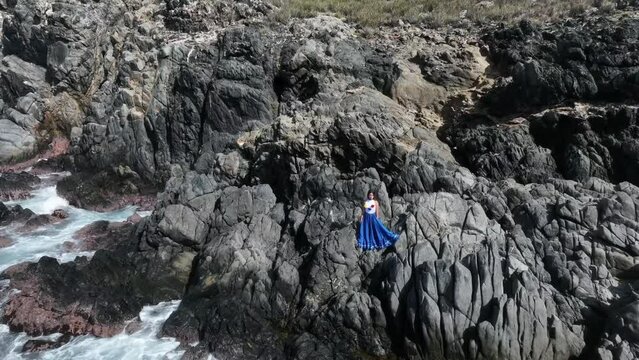 Camera quickly approaches young lady in national style dress standing on rocks at the coast of Gran Roque Island in Los Roques Archipelago, Venezuela.