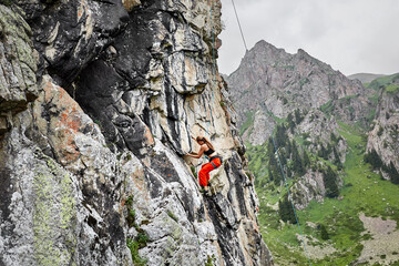 Woman athlete climbing on the high rock in the mountains