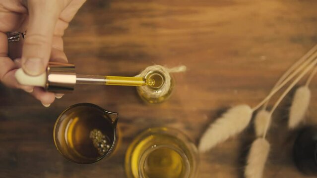 Extracts from natural oils. Work at home. View from above. Women's hands and a pipette with oil. Drop. Self made. Authenticity. Wooden table. Craft. Production of natural cosmetics.