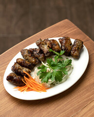 Shish kebab pieces on plate with vegetable garnish. Fried meat slices with onions and carrots. Plate with dish on wooden table. Dinner at restaurant. Top view. Copis pace. 