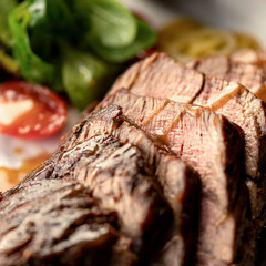 Well-done beef steak cut into pieces. Meat on plate with vegetables and herbs. Grilled steak. Grill menu. Close-up. View from above. Soft focus.