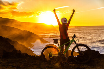 Fototapeta Success, achievement, accomplishment and winning concept with cyclist mountain biking. Winning happy MTB woman cycling reaching goal raising arms at sunset cheering and celebrating at summit top. obraz