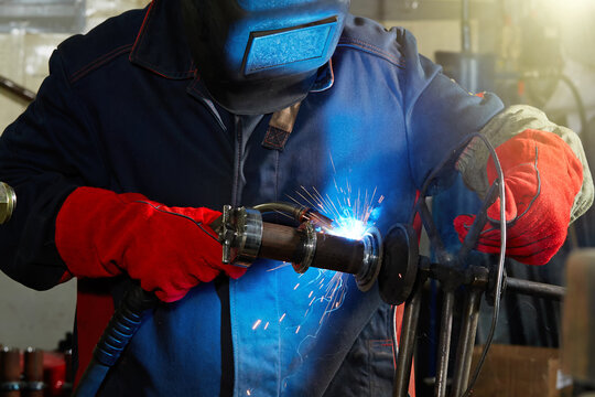 A welder wearing a protective mask and red gloves