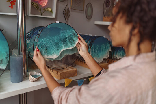 Woman decorator puts handmade epoxy resin glass tray with sea waves on stand in art studio