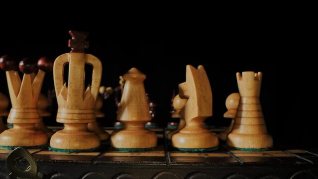 Chess game. A wooden chess pieces on a chess board in lights and shadows. Black background.
