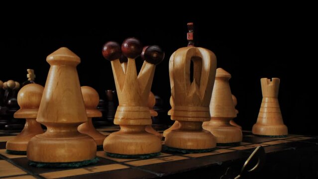 Chess game. A wooden chess pieces on a chess board in lights and shadows. Black background.