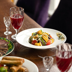 Lunch at restaurant for two people. Salad, cold appetizers, glasses with fruit drinks and glasses on table. Wooden table, purple armchair. Soft focus. Side view. 