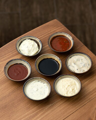 Several different types of sauces in round gravy boats on wooden table. Ketchup, soy sauce, tomato sauce, mayonnaise, sour cream sauce, white sauce. Basic types of sauces View from above. Copy space.