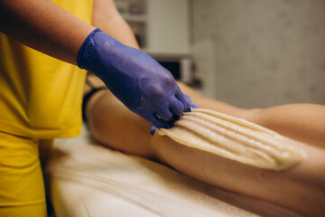 Beautician in gloves applying green hot wax on woman buttocks using spatula.