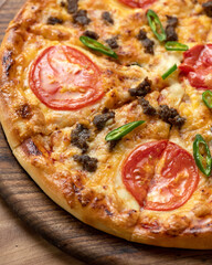 Pizza slice with tomatoes, cheese and minced meat. Pizza is cut into slices on wooden board. Italian Cuisine. Fast food. Wooden background. Close-up. Top view. Soft focus. 