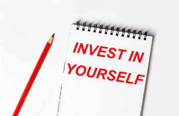 Red pencil and white notepad with the text INVEST IN YOURSELF
