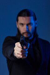 Looking like John Wick. Studio portrait of bearded young man with gun, dressed as a spy or secret agent.