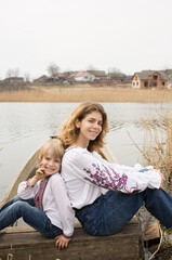 happy little boy and young beautiful woman in embroidered national clothes sit next to each other on shore of lake. Family, refugees, unity, support, freedom, independence. Ukrainians against the war